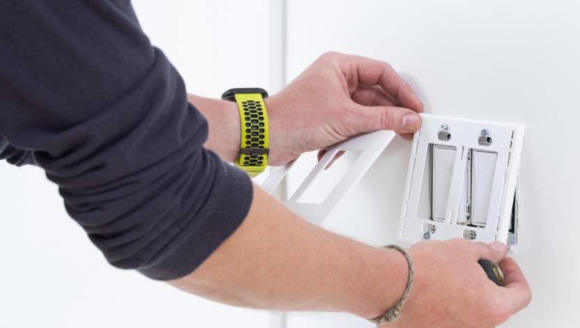 Person installing a double light switch with a screwdriver, aligning the wall plate on a white wall.