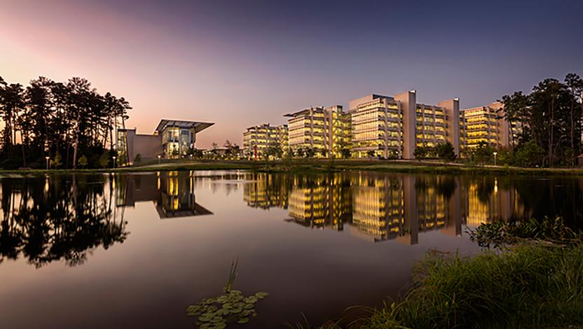 Modern commercial campus illuminated at dusk, with building lights reflecting on a lake.