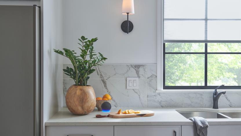 Kitchen with a marble backsplash, potted plant, countertop cutting board, and window shades filtering natural light.