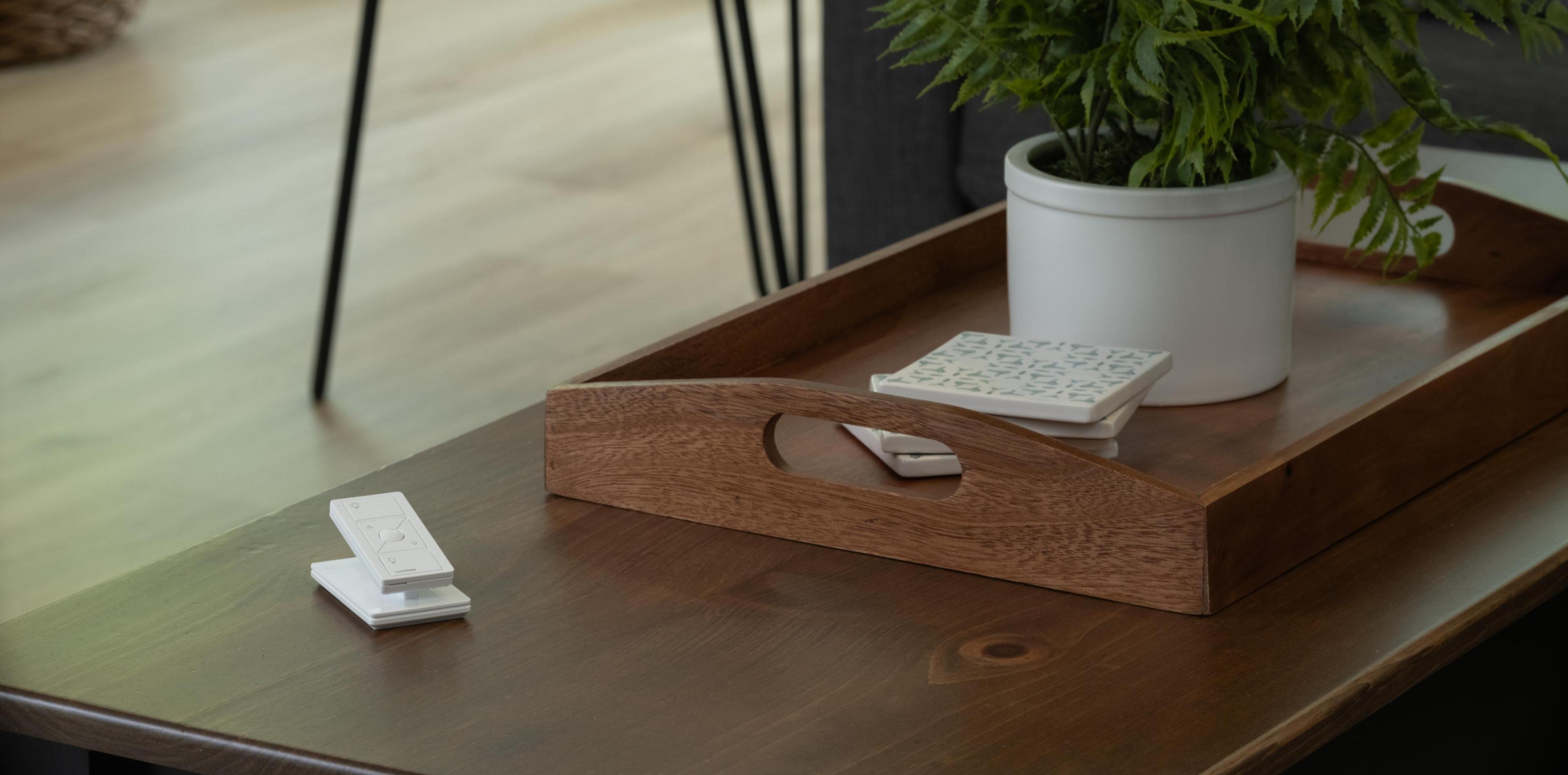 Close-up of a wooden coffee table with a potted fern, coasters, and a smart remote control in a cozy living room