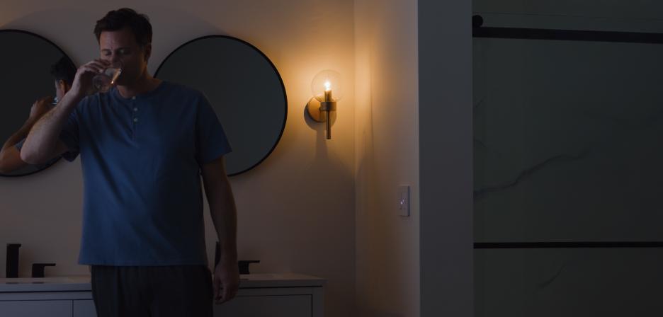 Man drinking water in a bathroom beside a softly glowing Diva dimmer with Night Mode.