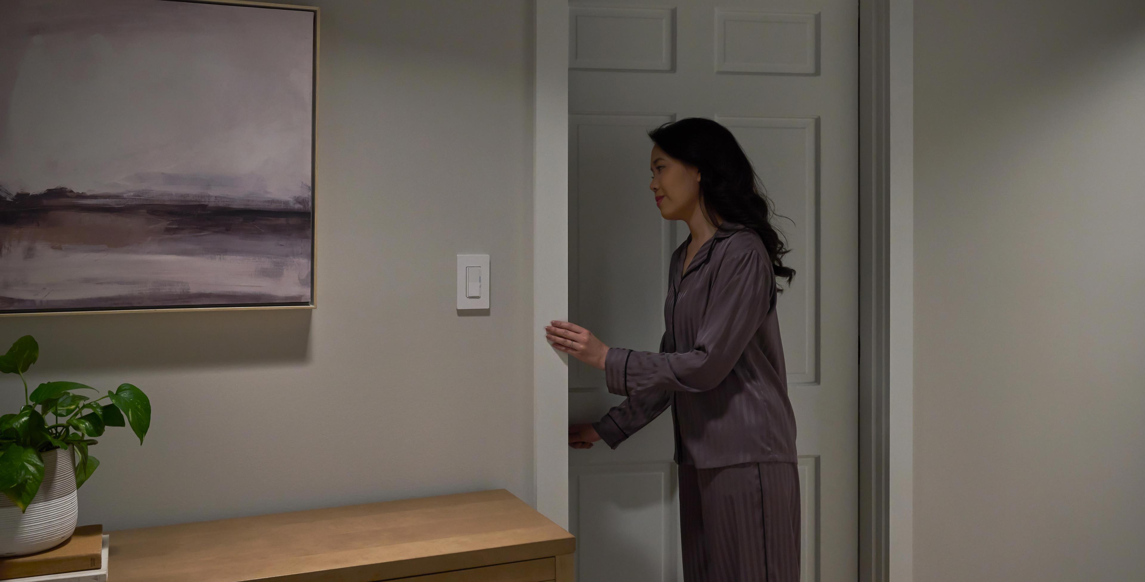 The Diva dimmer with Night Mode casts a soft glow as a woman walks in the hallway at night.