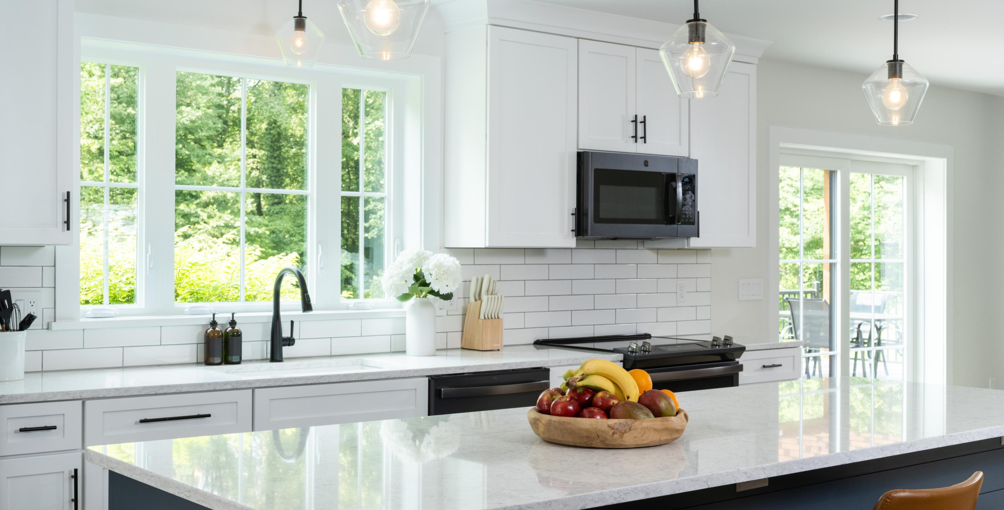 Bright modern kitchen with white cabinets, black fixtures, pendant lighting, and a fruit bowl on a large island countertop