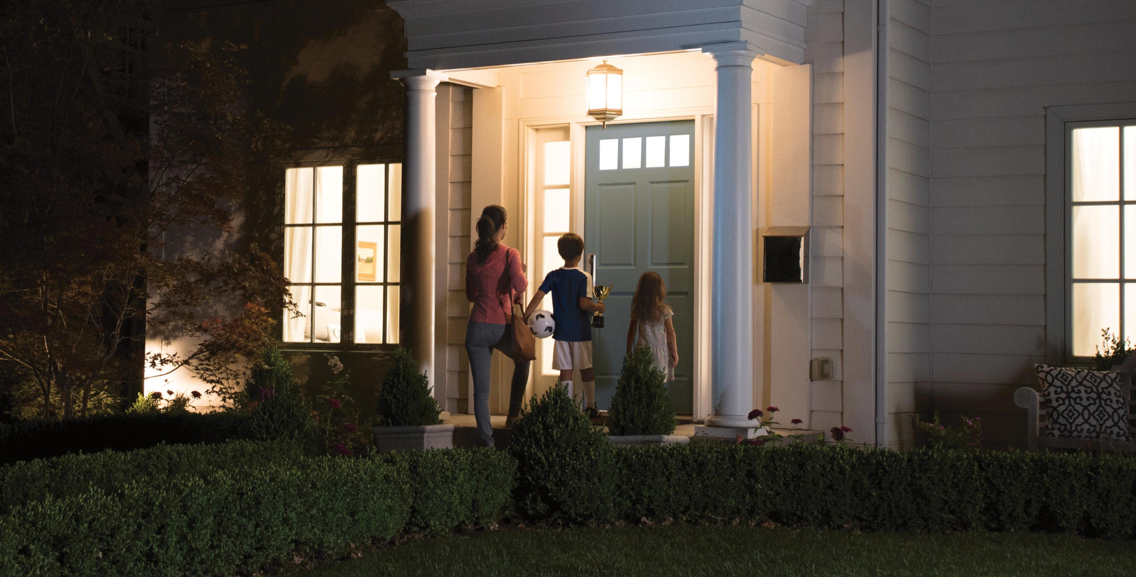A young family arrives home at night to a well-lit house.