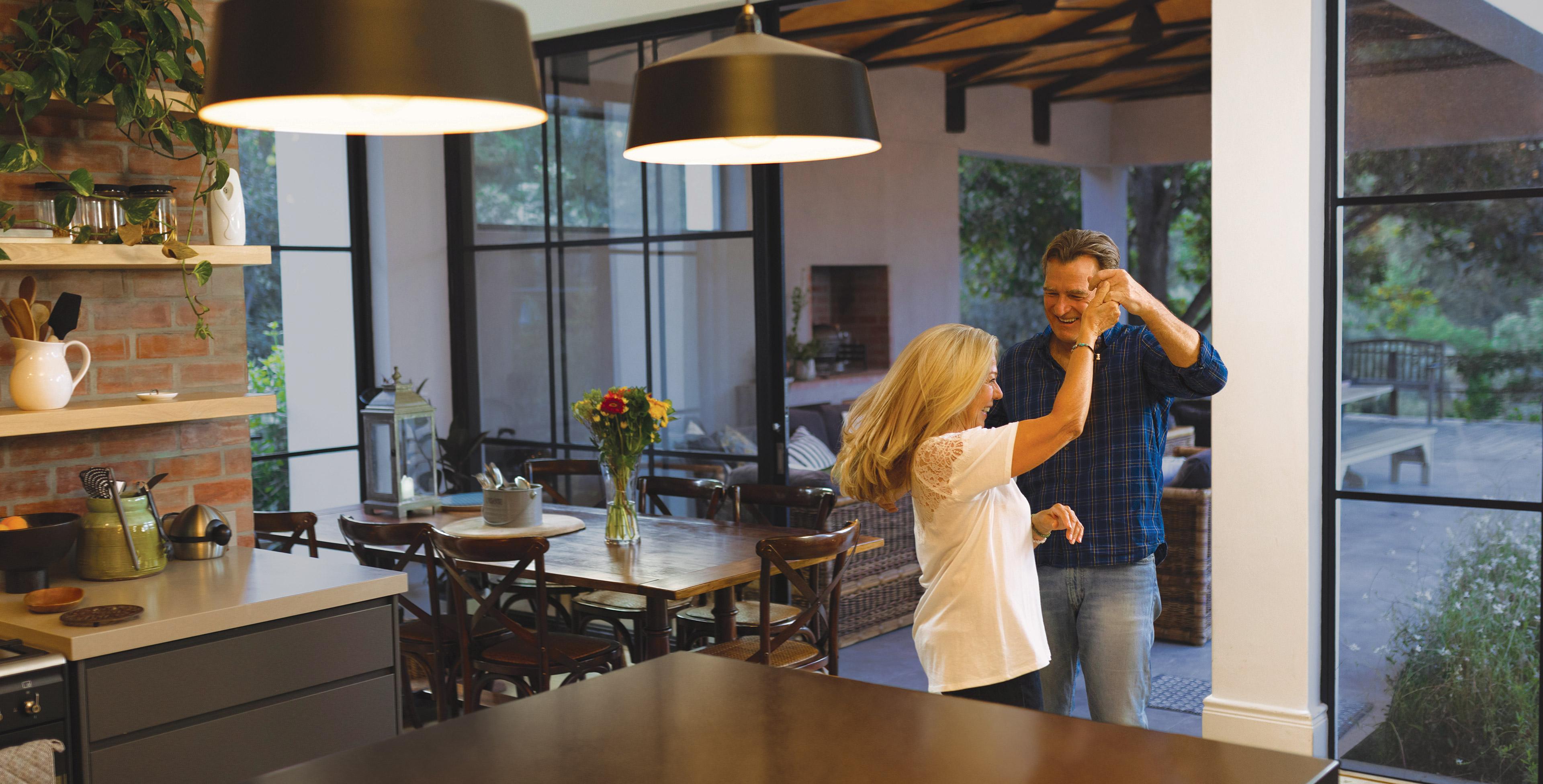 Couple dancing in an open-plan kitchen under warm-dim fixture lights.