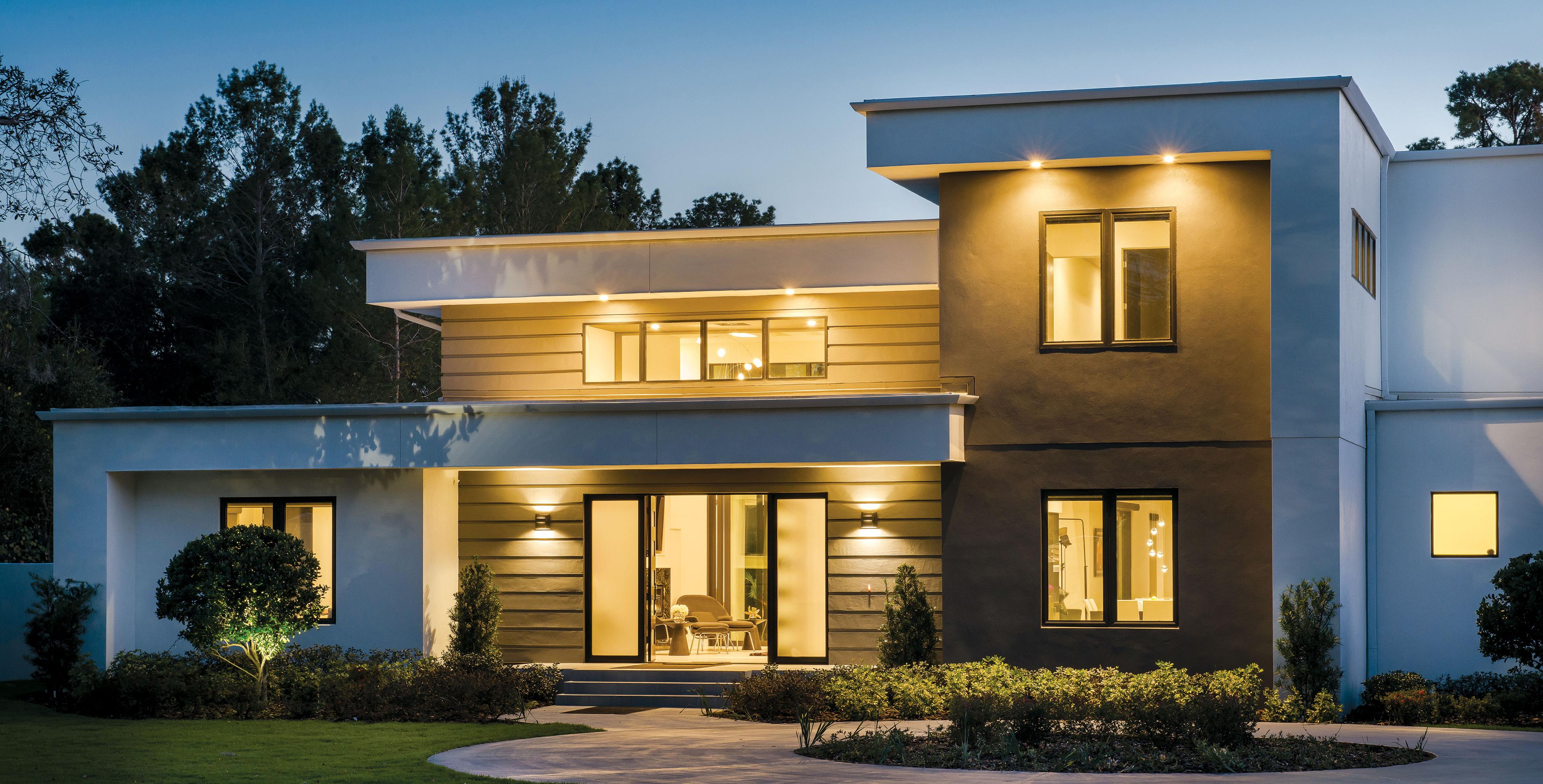 Two-story mansion at dusk with brightly lit interior.