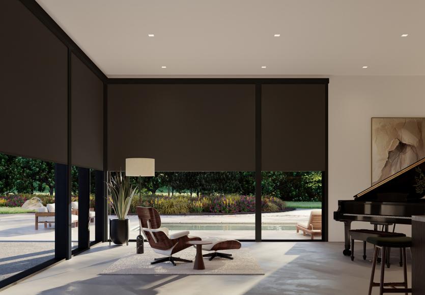 Living room with floor-to-ceiling windows fitted with blackout roller shades that block exterior light and darken the space completely.