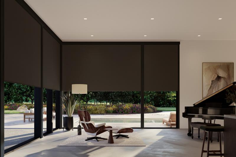 Living room with floor-to-ceiling windows fitted with blackout roller shades that block exterior light and darken the space completely.