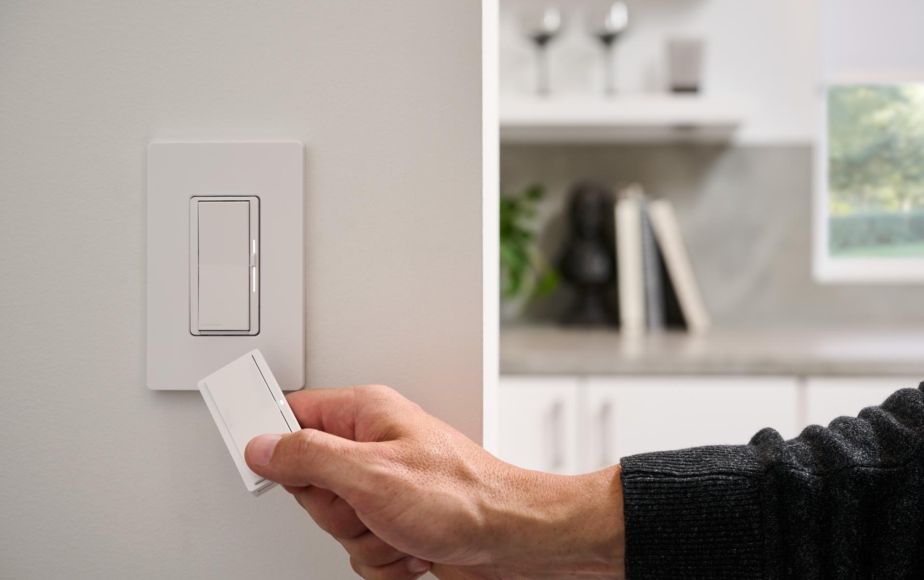 Close-up of hand holding a Pico remote in front of a paddle-style Sunnata dimmer and switch.